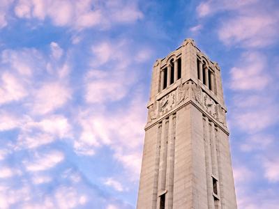 The NC State Memorial Belltower rises into a sky of puffy clouds just after sunrise. Photo by Becky Kirkland.