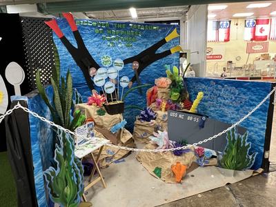 Underwater-themed display with coral, sign reading "USS NC BB-55" and blue backdrop