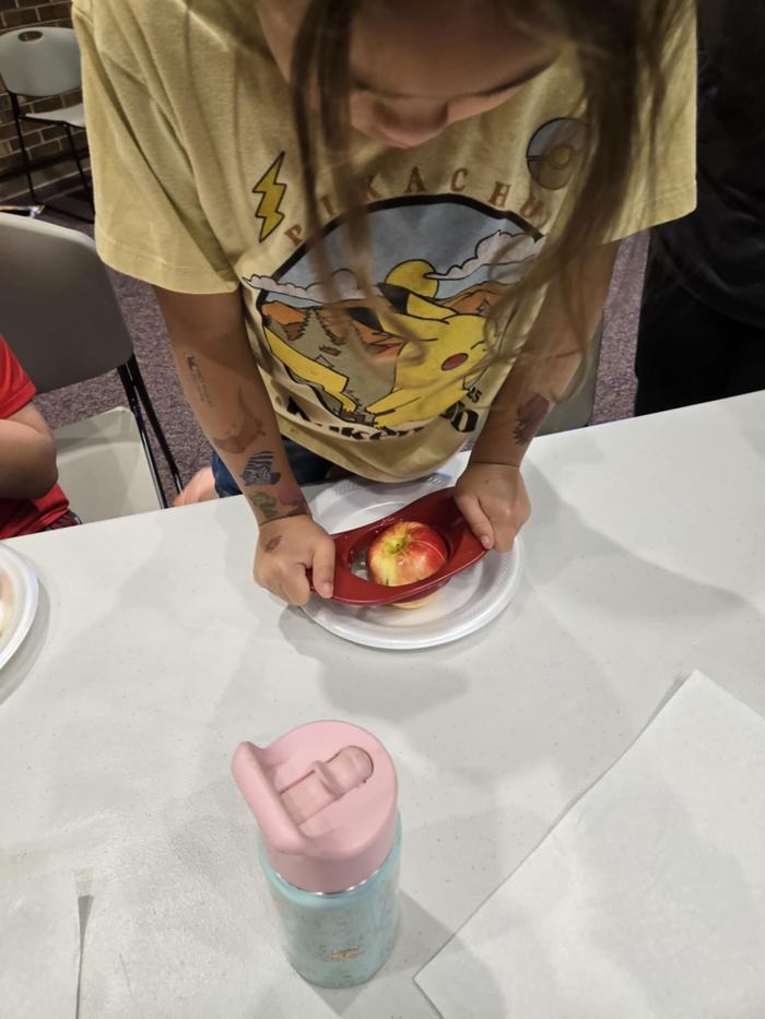 A student uses an apple slicer on a red apple.