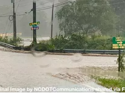 Flooded roadway with water covering lanes, guardrail visible and emergency lights ahead