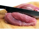 Raw pork tenderloin slices on wooden cutting board with a chef's knife