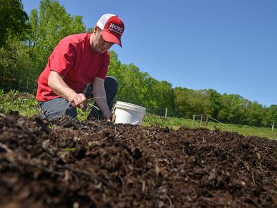 An NC State student tends to soil in a farm field.