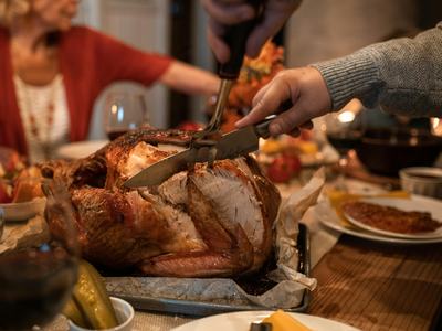 image of hands holding utensils while carving a turkey