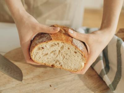 Hands holding a halved loaf of crusty bread over a cutting board