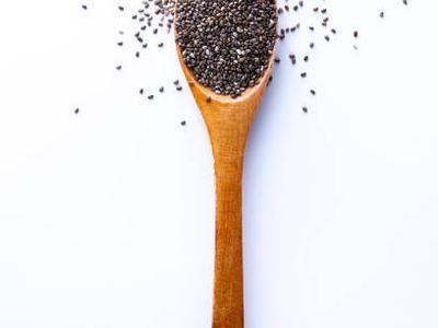 Flat lay of wooden spoon filled with small seeds of chia lying on white background