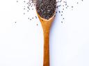 Flat lay of wooden spoon filled with small seeds of chia lying on white background