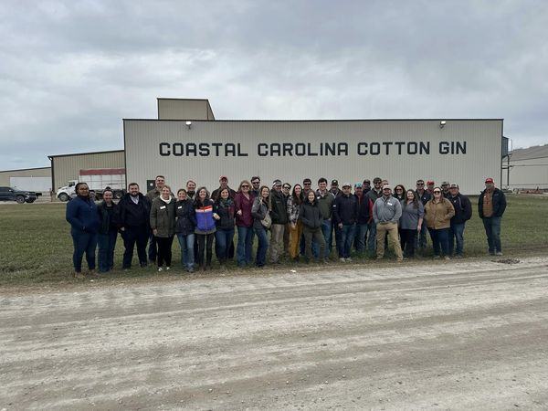 Group of about 40 people standing in front of a building labeled "COASTAL CAROLINA COTTON GIN"