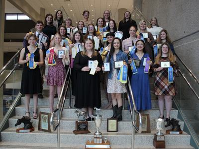 Group of students on stairs holding plaques, ribbons, and trophies
