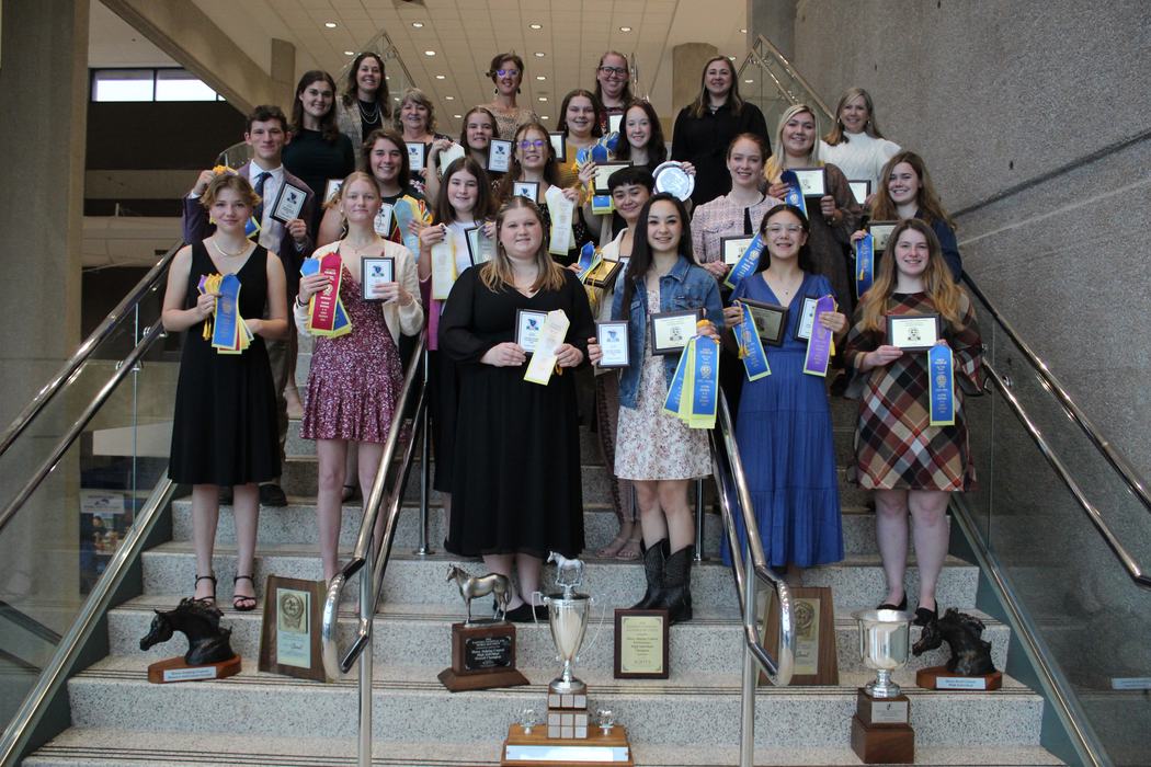 Group of students on stairs holding plaques, ribbons, and trophies