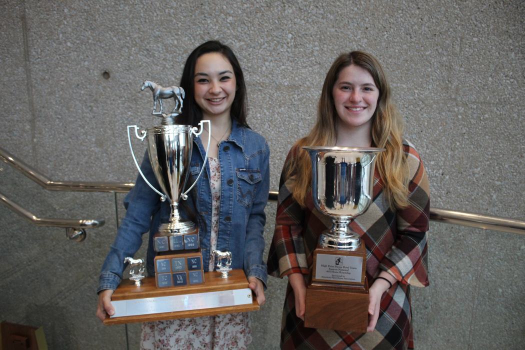 Two people standing side-by-side holding large silver trophies