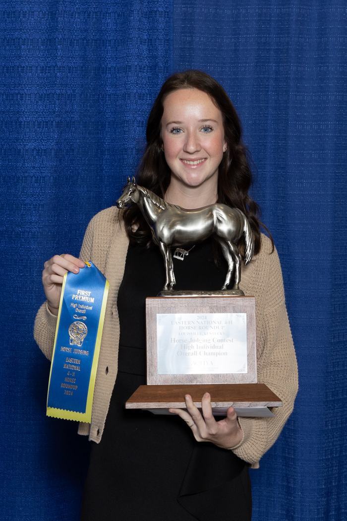 Young woman holding horse trophy and blue ribbon reading "FIRST PREMIUM"