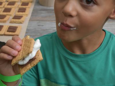 Boy holding and eating two s'mores, marshmallow visible on his lips