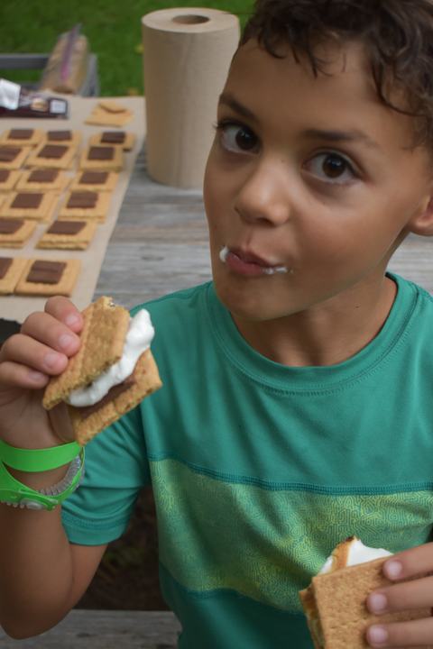 Boy holding and eating two s'mores, marshmallow visible on his lips