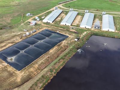 Aerial farm view with black-covered lagoon beside barns and an aerated wastewater pond