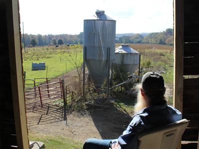 A man sits in a barn looking out at his farm.