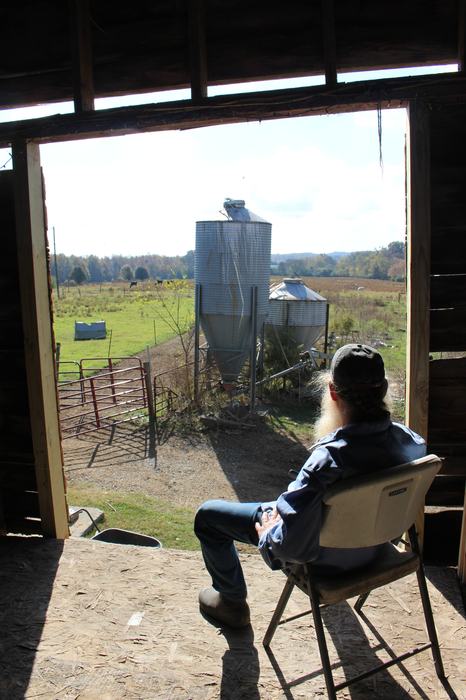 A man sits in a barn looking out at his farm.