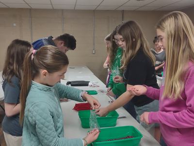 Several students sorting beads into green trays and filling small plastic bags