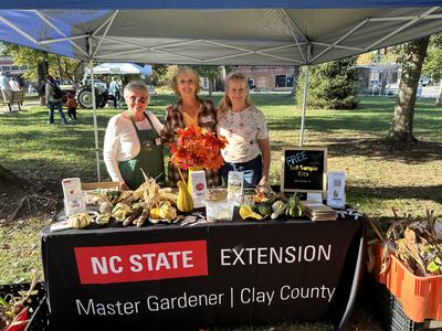 Three women at NC STATE Extension Master Gardener booth with gourds and "FREE Soil Sample Kits" sign