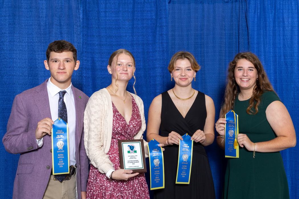 Four young adults holding blue "First Premium" ribbons and a plaque against a blue curtain