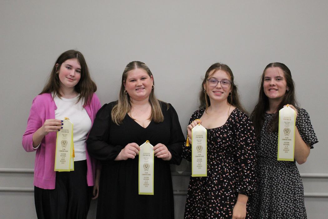 Four young women standing side-by-side holding yellow ribbons reading "Fourth Premium"
