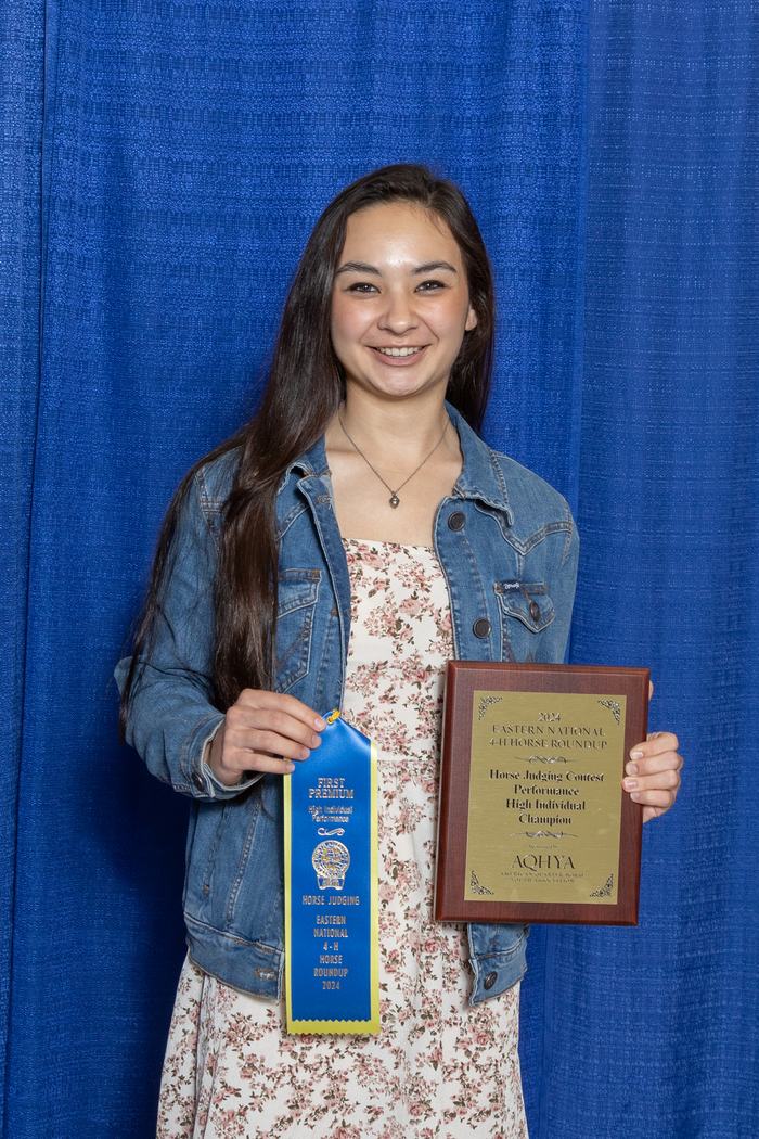 Young woman holding blue ribbon "FIRST PREMIUM" and plaque reading "Horse Judging Contest High Individual Champion"