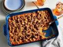 Rectangular blue baking dish with fruit crumble, one portion scooped out and serving spoon