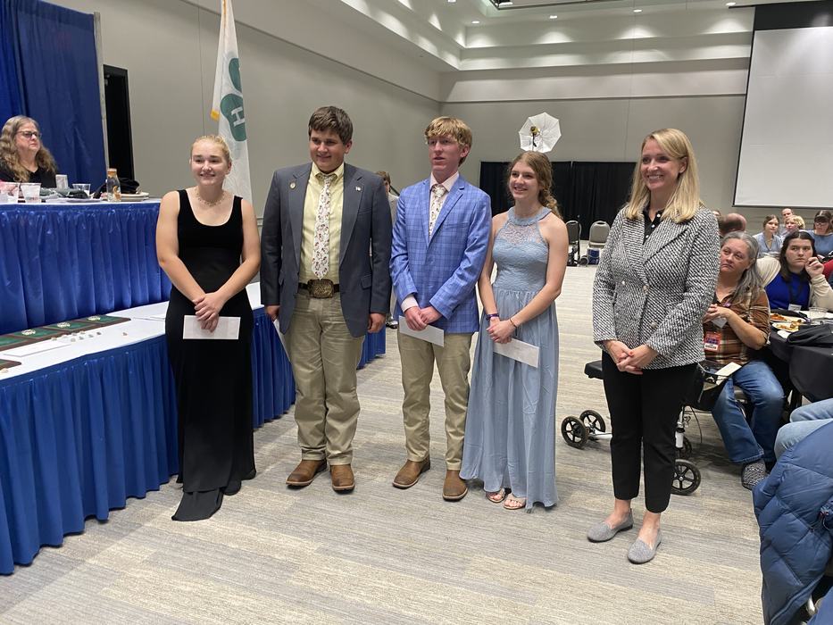 Four teens holding envelopes and one adult standing in a line at an indoor awards event