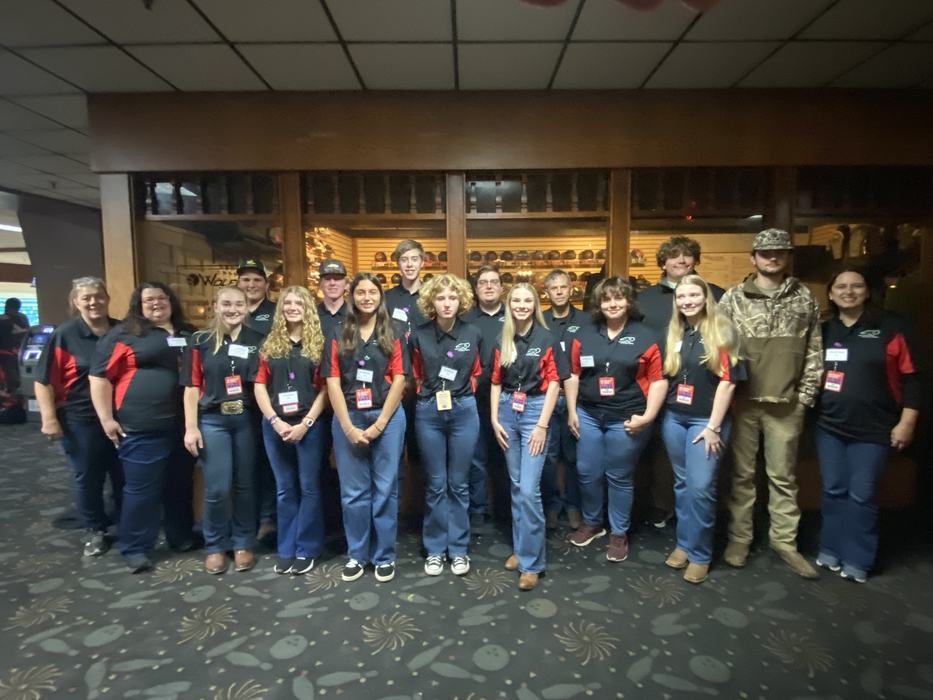 Seventeen people in matching black and red shirts posing inside a bowling alley