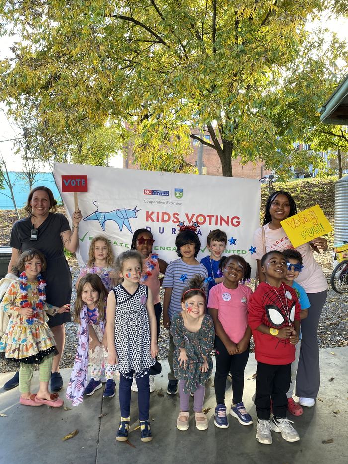 A group of children standing in front of a Kids Voting Sign.
