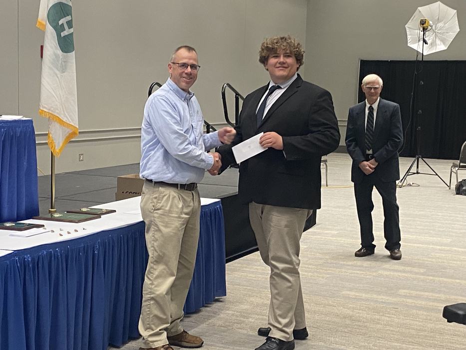 Young man in suit receives an envelope and shakes hands with a man at an awards table