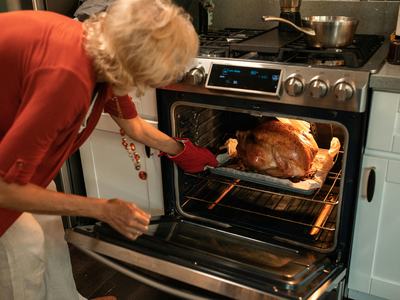 person bent over removing cooked turkey from an open oven