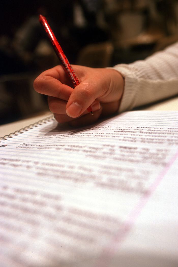 Hand holding red pen writing in spiral notebook filled with handwritten notes
