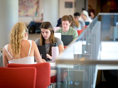 Two students seated across a table using laptops in a campus study area