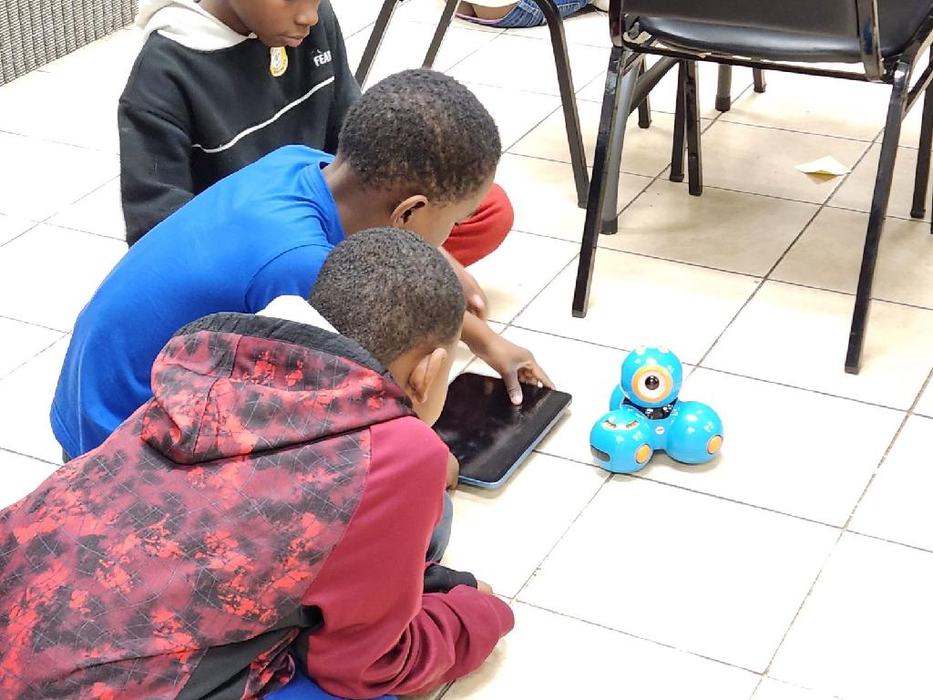 Students play with a blue robot on the floor.