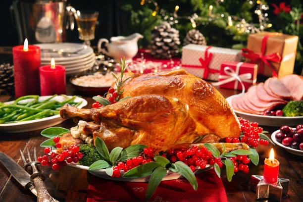 Christmas turkey dinner. Baked turkey garnished with red berries and sage leaves in front of Christmas tree and burning candles