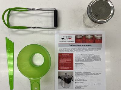 printed paper titled canning low acid foods alongside canning tools on kitchen countertop