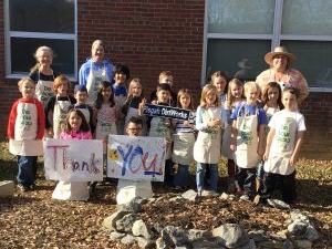 Group of children and adults in aprons outdoors holding painted "THANK YOU" sign