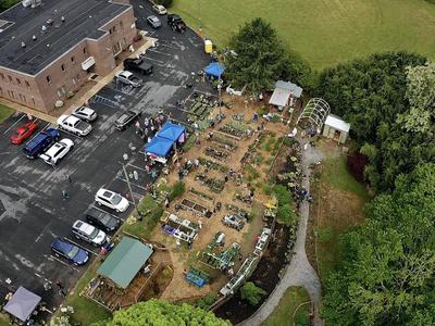 Aerial view of community garden with people, vendor tents, and adjacent parking lot
