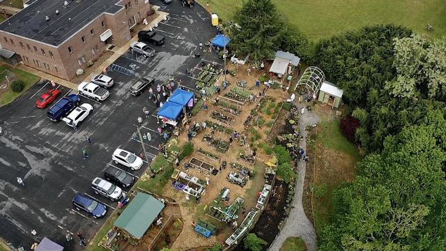 Aerial view of community garden with people, vendor tents, and adjacent parking lot