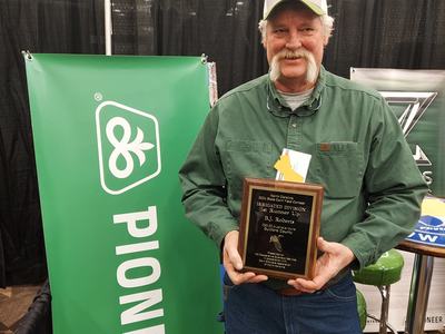 Man in green shirt holding an award plaque at a booth with a vertical "PIONEER" banner