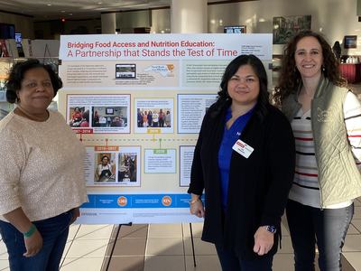 Three women standing in front of a poster titled "Bridging Food Access and Nutrition Education"