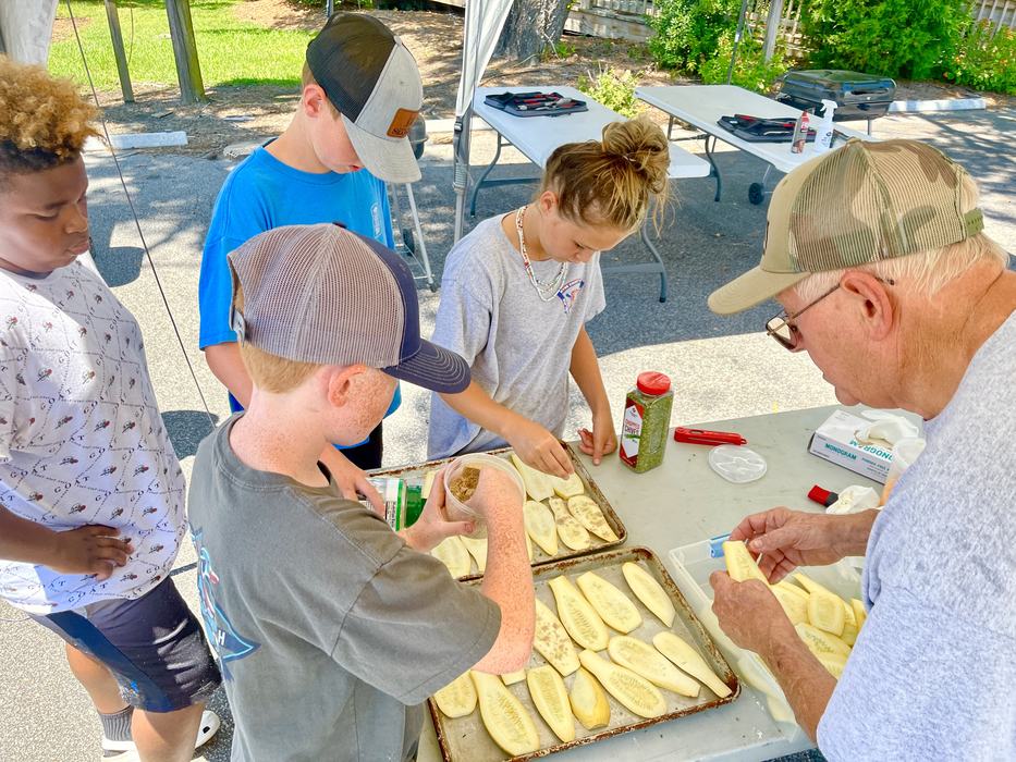 Children and older man arranging sliced squash on baking trays at an outdoor table