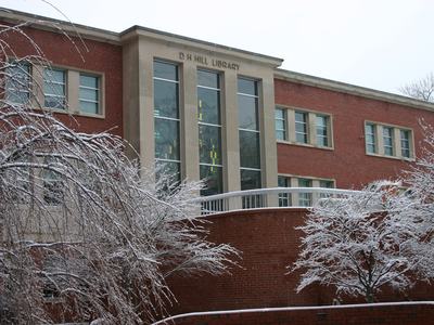 D H Hill Library facade with snow-covered trees and brick retaining wall