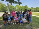 Group of children and adults posing on grass by a basketball hoop outdoors