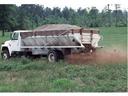 White spreader truck dispersing granular material across a grassy field