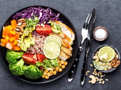 Buddha bowl dish with chicken fillet, brown rice, avocado, pepper, tomato, broccoli, red cabbage, chickpea, fresh lettuce salad, pine nuts and walnuts. Healthy balanced eating. Top view