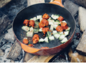 Orange skillet on wood with diced zucchini and chorizo cooking