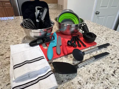 Assorted kitchen utensils on granite countertop: mixing bowls, knives, measuring spoons, towels
