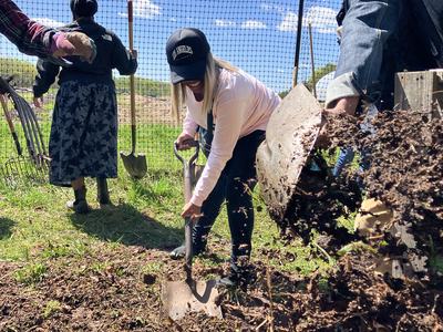 Three people shoveling and spreading soil near a fenced garden; hat reads "LOS ANGELES"