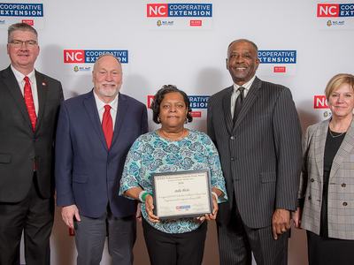 Woman holding framed award labeled NC Cooperative Extension, flanked by four people